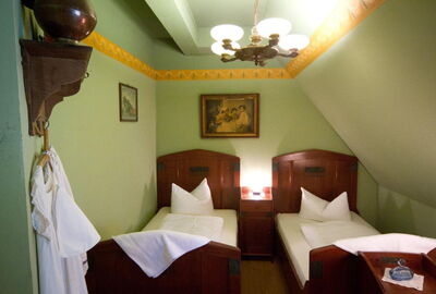 Blick auf die beiden Einzelbetten in der Mitte ein Beistelltisch. Mittelalterliches Flair durch historische Möbel in dunklem Holz und Wanddeko. Hellgrüne Wände mit gelber Bordüre.