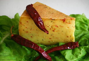 Zu sehen ist ein St?ck K?se mit roten Chiliflocken