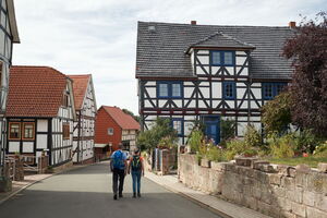 Zwei Wanderer auf dem P16 in Asbach-Sickenberg mit idyllischen Fachwerkhäusern und Höfen.