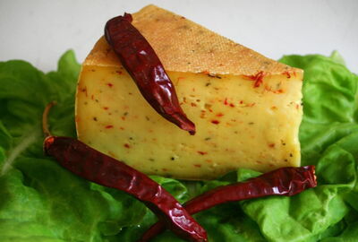 Zu sehen ist ein St?ck K?se mit roten Chiliflocken