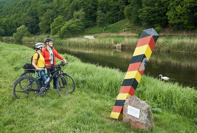 Zwei Radfahrer am Werratalradweg in Lindewerra mit Grenzstele der ehemeligen innerdeutschen Grenze am grünen Band