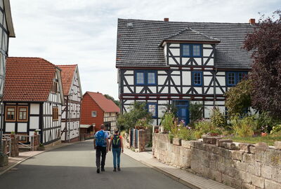 Zwei Wanderer auf dem P16 in Asbach-Sickenberg mit idyllischen Fachwerkhäusern und Höfen.