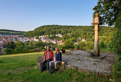 zwei Wanderer machen Pause am Bildstock oberhalb von Heyerode im Eichsfeld
