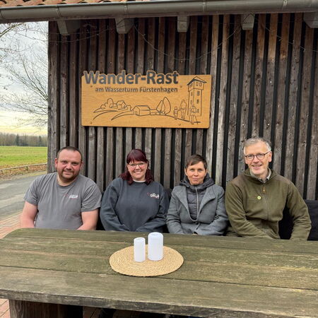 Vier Personen sitzen an einem Holztisch unter dem Schild "Wander-Rast"